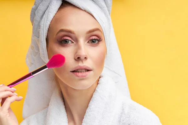 Zbliżenie piękna kobieta robi makijaż z za pomocą pędzla izolowane na żółtym tle — Zdjęcie stockowe