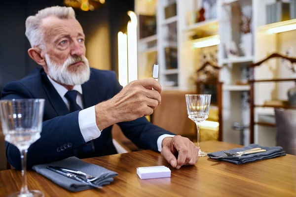 Porträtt senior man gråhårig sitta i restaurang ser elektronisk cigarett — Stockfoto