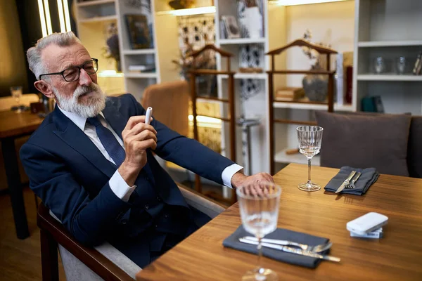 Hombre mayor guapo en traje humo cigarrillo electrónico en el restaurante — Foto de Stock