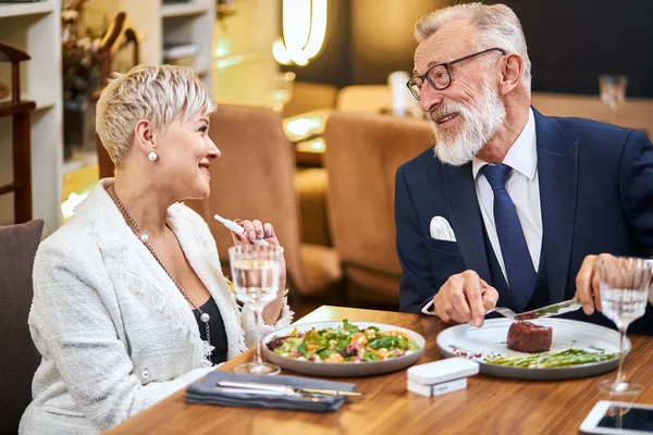 Senior pareja moderna tomando una comida en el restaurante usando IQOS, cigarrillo electrónico — Foto de Stock