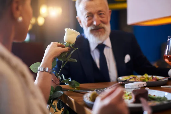 Milující muž předvádí bílou květinu své ženě. Pár slaví výročí v restauraci — Stock fotografie