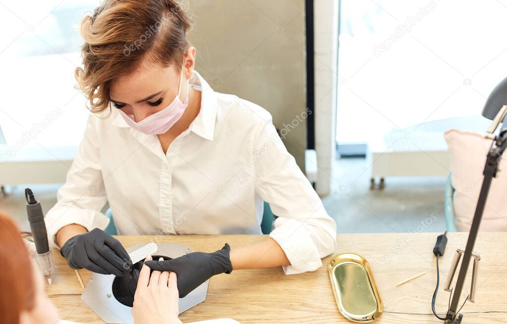 Nails salon woman in white do manicure