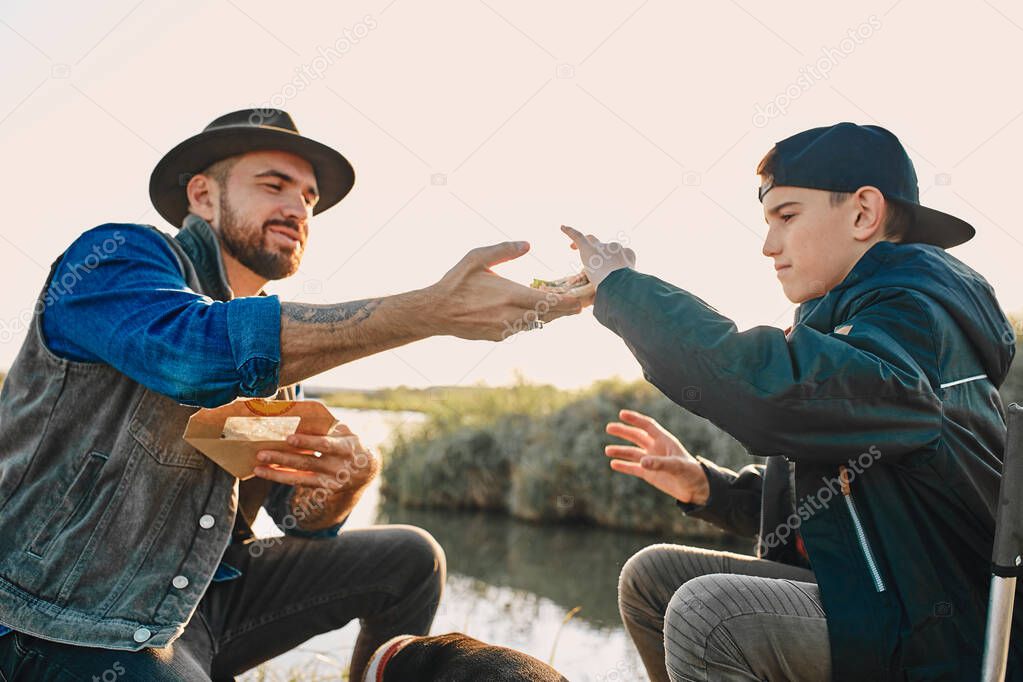 The first joint fishing of adult father and teen son in warm, sunny day.