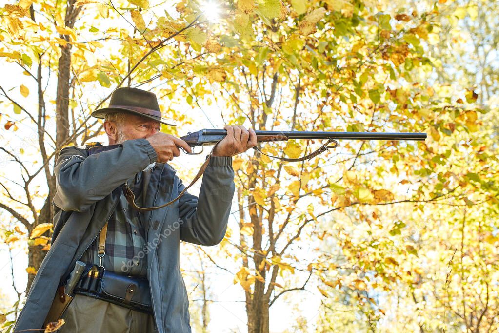 Senior hunter with his rifle in autumn forest