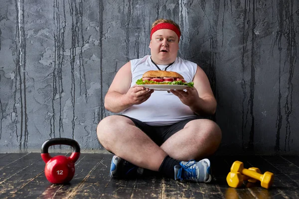 Otyły facet będzie jeść Duży kanapka pomimo niedawnego treningu sportowego — Zdjęcie stockowe