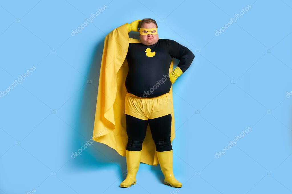 Thoughtful fat caucasian superhero isolated over blue background, man is in contemplation.