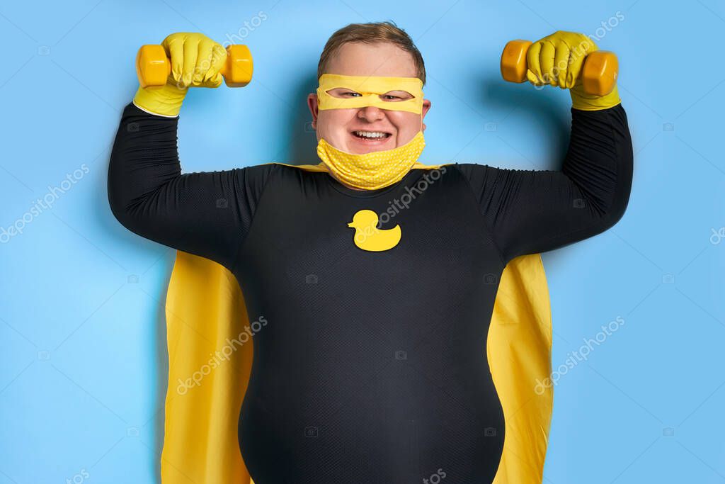 Strong fat caucasian superhero man shows his muscles at camera, young male in yellow wear has powerful energy, save the universe