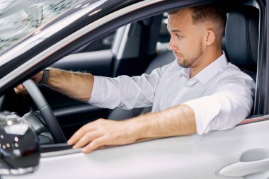 Yeni arabanın direksiyonunda oturan yakışıklı beyaz adamın portresi.