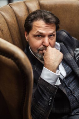Sakallı iş adamı deri koltukta otururken önemli şeyleri düşünür..