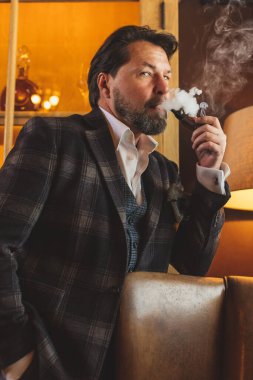İyi giyimli, gözlüklü, tütün piposu içen olgun sakallı adam.