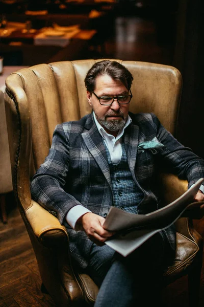 Man van middelbare leeftijd goed gekleed zittend in een fauteuil in de woonkamer leest de krant — Stockfoto