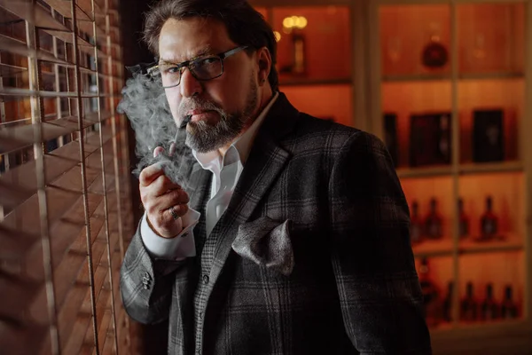 Reflexivo hombre barbudo maduro bien vestido en gafas fumar pipa de tabaco —  Fotos de Stock