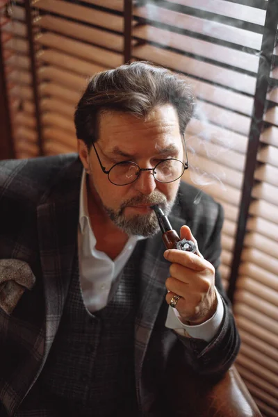 Світловідбиваюча добре одягнена зріла бородата людина в окулярах для куріння тютюнової труби — стокове фото