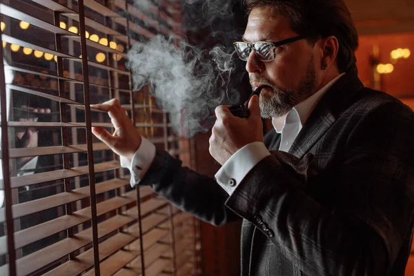 Світловідбиваюча добре одягнена зріла бородата людина в окулярах для куріння тютюнової труби — стокове фото