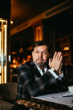 Sakallı iş adamı deri koltukta otururken önemli şeyleri düşünür..