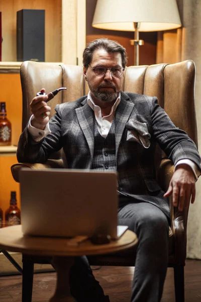 Editor creativo reflexionando sobre el nuevo artículo, sentado con el ordenador portátil, pipa de fumar — Foto de Stock