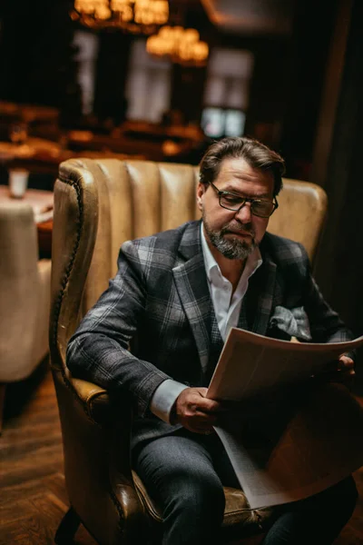 Hombre bien vestido de mediana edad sentado en el sillón en la sala de estar lee el periódico — Foto de Stock