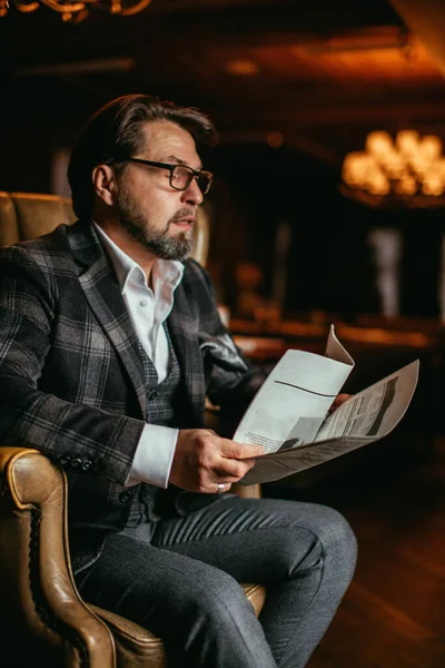 Hombre bien vestido de mediana edad sentado en el sillón en la sala de estar lee el periódico —  Fotos de Stock