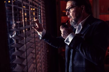 İyi giyimli, gözlüklü, tütün piposu içen olgun sakallı adam.