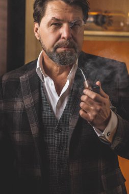 İyi giyimli, gözlüklü, tütün piposu içen olgun sakallı adam.