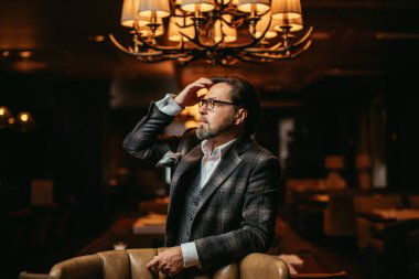 Sakallı iş adamı deri koltukta otururken önemli şeyleri düşünür..