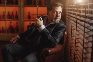 İyi giyimli, gözlüklü, tütün piposu içen olgun sakallı adam.