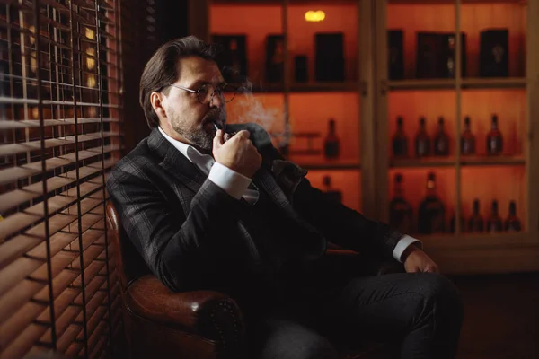 Reflecterende goed geklede volwassen bebaarde man in glazen roken tabakspijp — Stockfoto