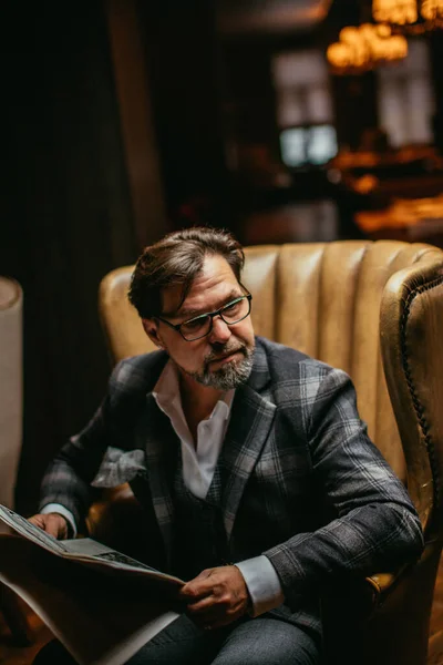 Hombre bien vestido de mediana edad sentado en el sillón en la sala de estar lee el periódico — Foto de Stock