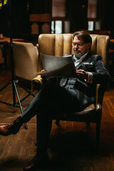Hombre bien vestido de mediana edad sentado en el sillón en la sala de estar lee el periódico — Foto de Stock
