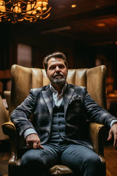 Pensativo elegante hombre de negocios barbudo piensa en algo importante mientras está sentado en el sillón de cuero en la sala de estar — Foto de Stock
