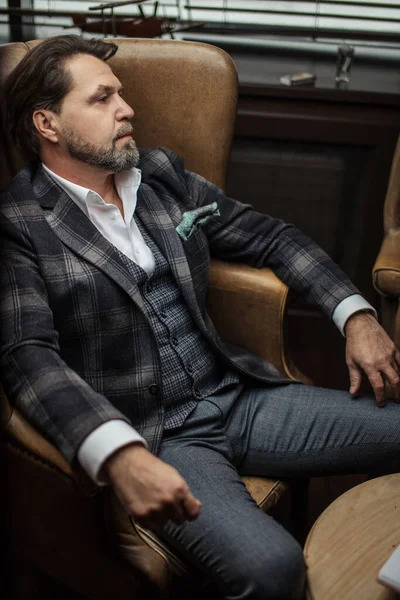 Empresario barbudo piensa en importante mientras está sentado en sillón de cuero . — Foto de Stock