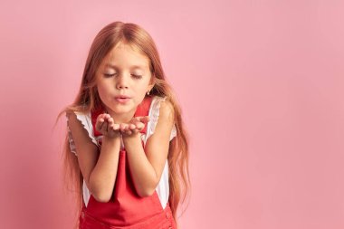 Çekici küçük kız pembe arka planda izole bir şekilde kameraya öpücük yolluyor.