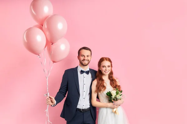 Retrato de belo casal jovem casamento de pé isolado sobre fundo rosa — Fotografia de Stock