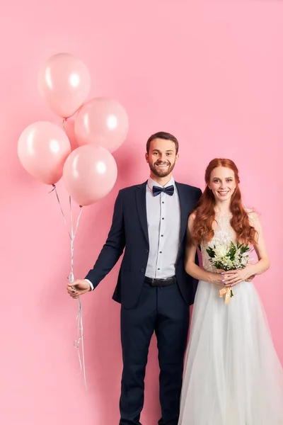Retrato de belo casal jovem casamento de pé isolado sobre fundo rosa — Fotografia de Stock