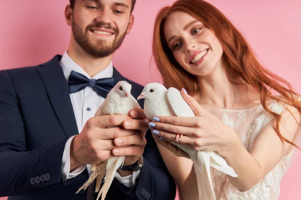 Casal jovem vestindo vestido de noiva e smoking segurar pombos nas mãos — Fotografia de Stock