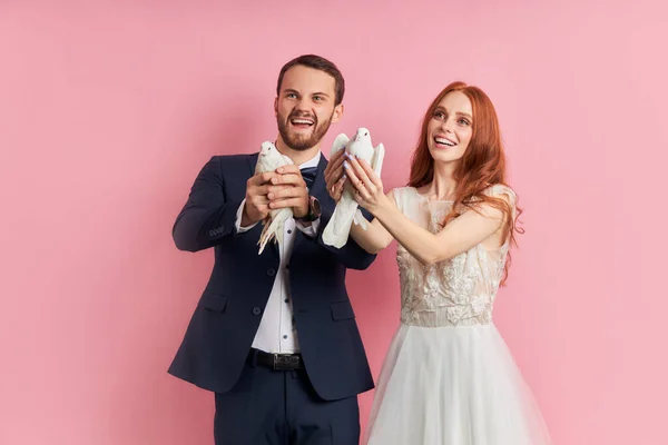 Casal jovem vestindo vestido de noiva e smoking segurar pombos nas mãos — Fotografia de Stock