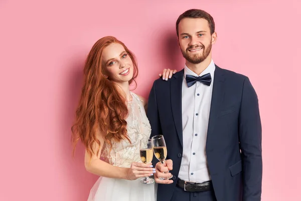 Lovely couple wearing white dress and tuxedo holding glass of champagne — Stock Photo, Image