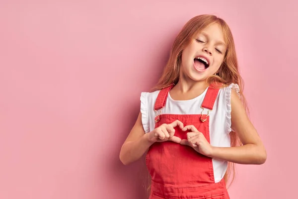 Vicces kislány show szív elszigetelt felett rózsaszín háttér — Stock Fotó