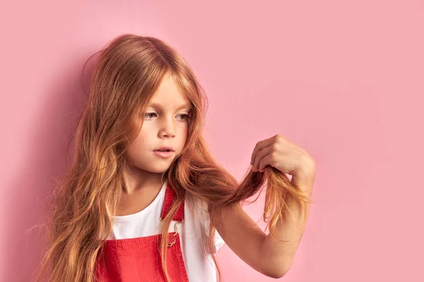 Niña preocupada mirando el pelo aislado sobre fondo rosa —  Fotos de Stock