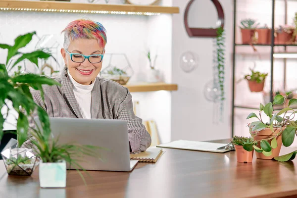 Улыбающаяся бизнесвумен средних лет в синих очках с помощью ноутбука — стоковое фото