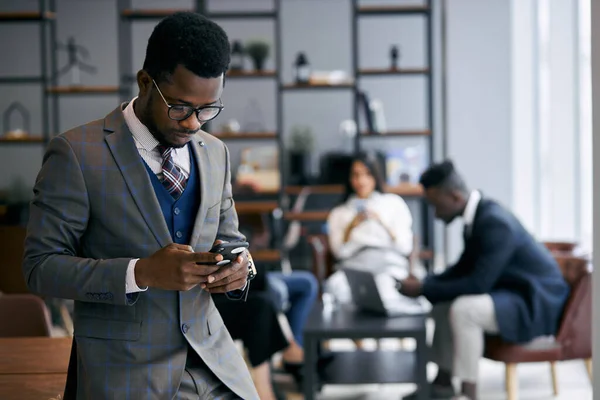 Elfoglalt, fiatal afrikai férfi mobiltelefont használ munka közben — Stock Fotó