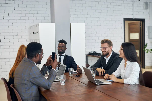 Молодые африканцы и кавказцы, сидящие в современном офисе и беседующие — стоковое фото