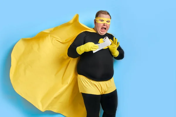 Portrét směšného tlusťocha v kostýmu superhrdiny s toaletním papírem v rukou — Stock fotografie