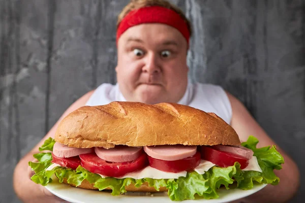 Człowiek z nadwagą wkracza na dużą wysokokaloryczną kanapkę — Zdjęcie stockowe