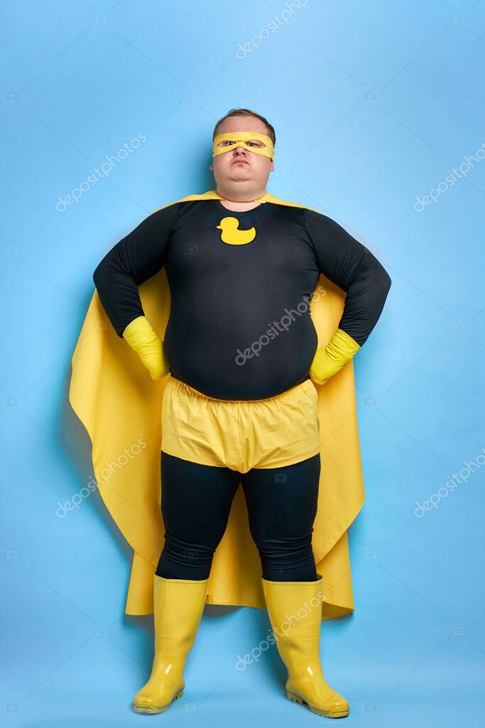 Cleaning superhero saves the world from dirt, man has duck picture on costume, he is in yellow wear and in protective gloves, posing isolated over blue background