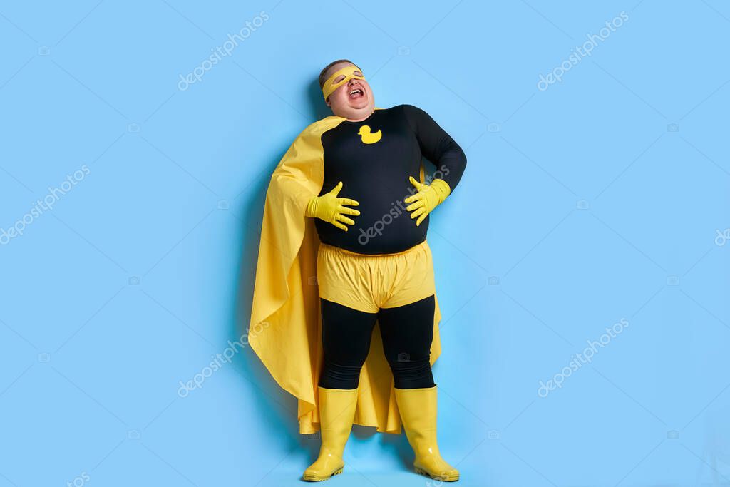 Happy corpulent caucasian man holding his stomach, man in superhero wearing posing at camera, laugh