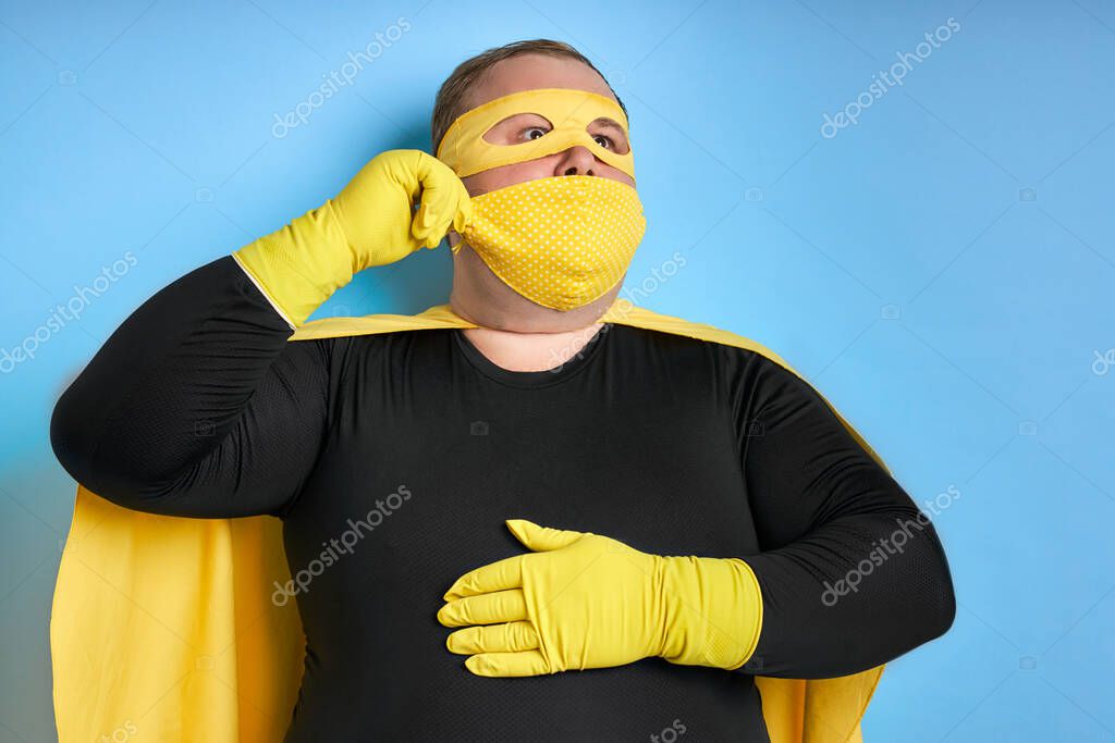 Handsome brave strong man has a mad desire, a dream to shield the world from dirt and evil. fat superhero in yellow costume posing isolated over blue background