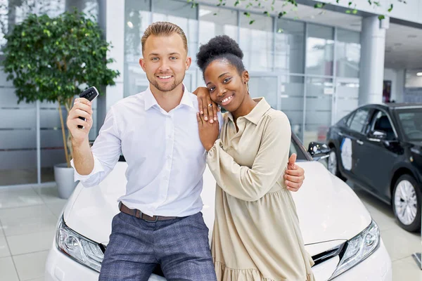 Caucasian man holds keys from his new car in dealership — Stock Photo, Image