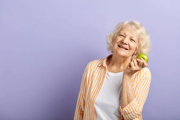 Šťastná usměvavá žena v šedesátých letech drží zelené jablko a usmívá se na kameru. — Stock fotografie