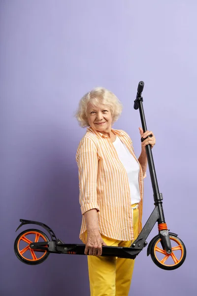 Une activité amusante. Joyeuse femme mature positive tenant scooter tout en posant à l'intérieur. — Photo